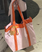 Pink tote bag with orange accents matching color with her Deng Patch Denim Pants.