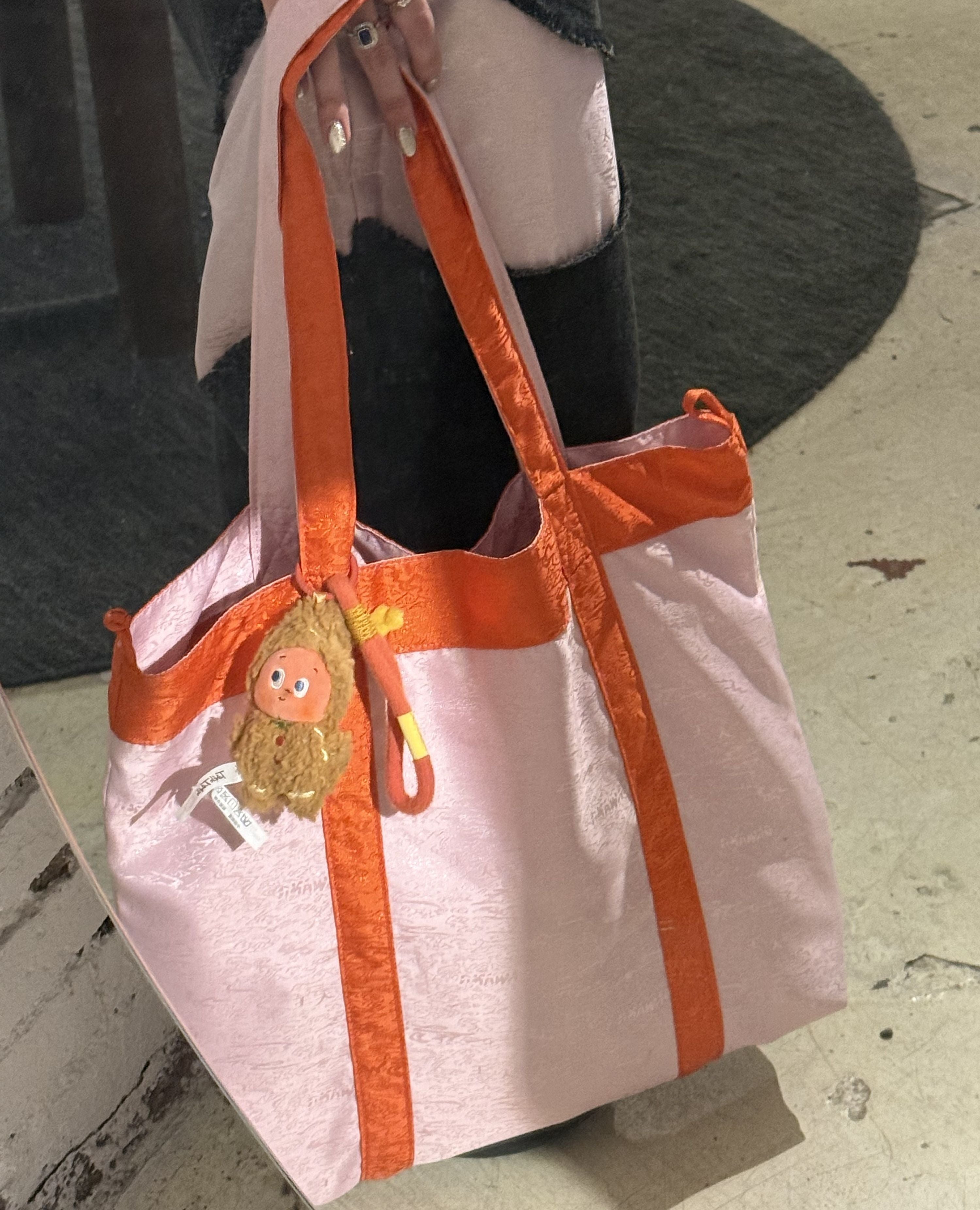Pink tote bag with orange accents matching color with her Deng Patch Denim Pants.