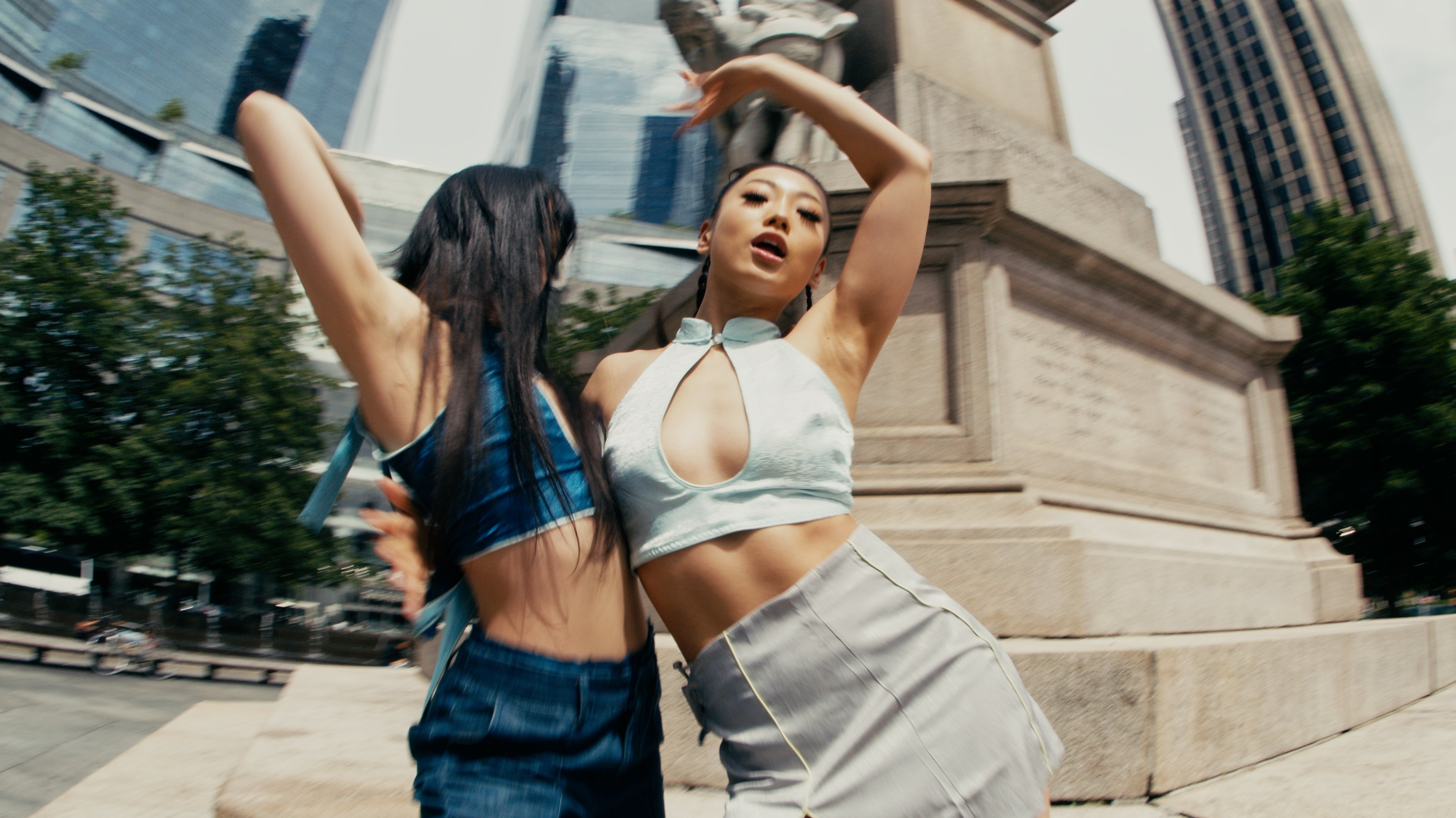 Two women dancing in an urban setting with tall buildings in the background